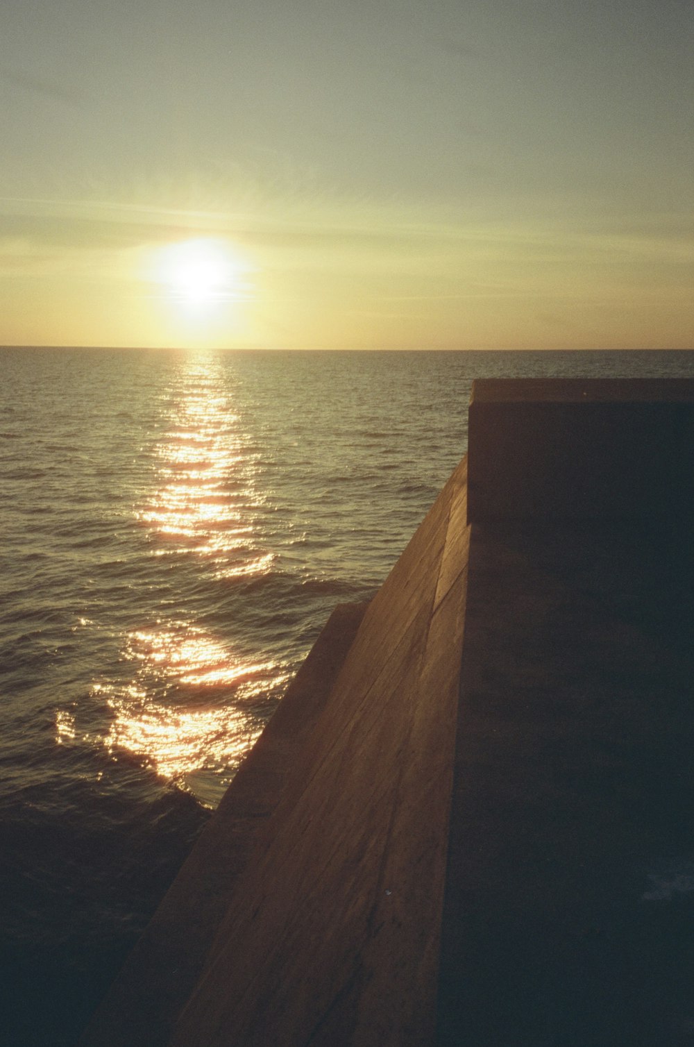 the sun is setting over the water from a pier