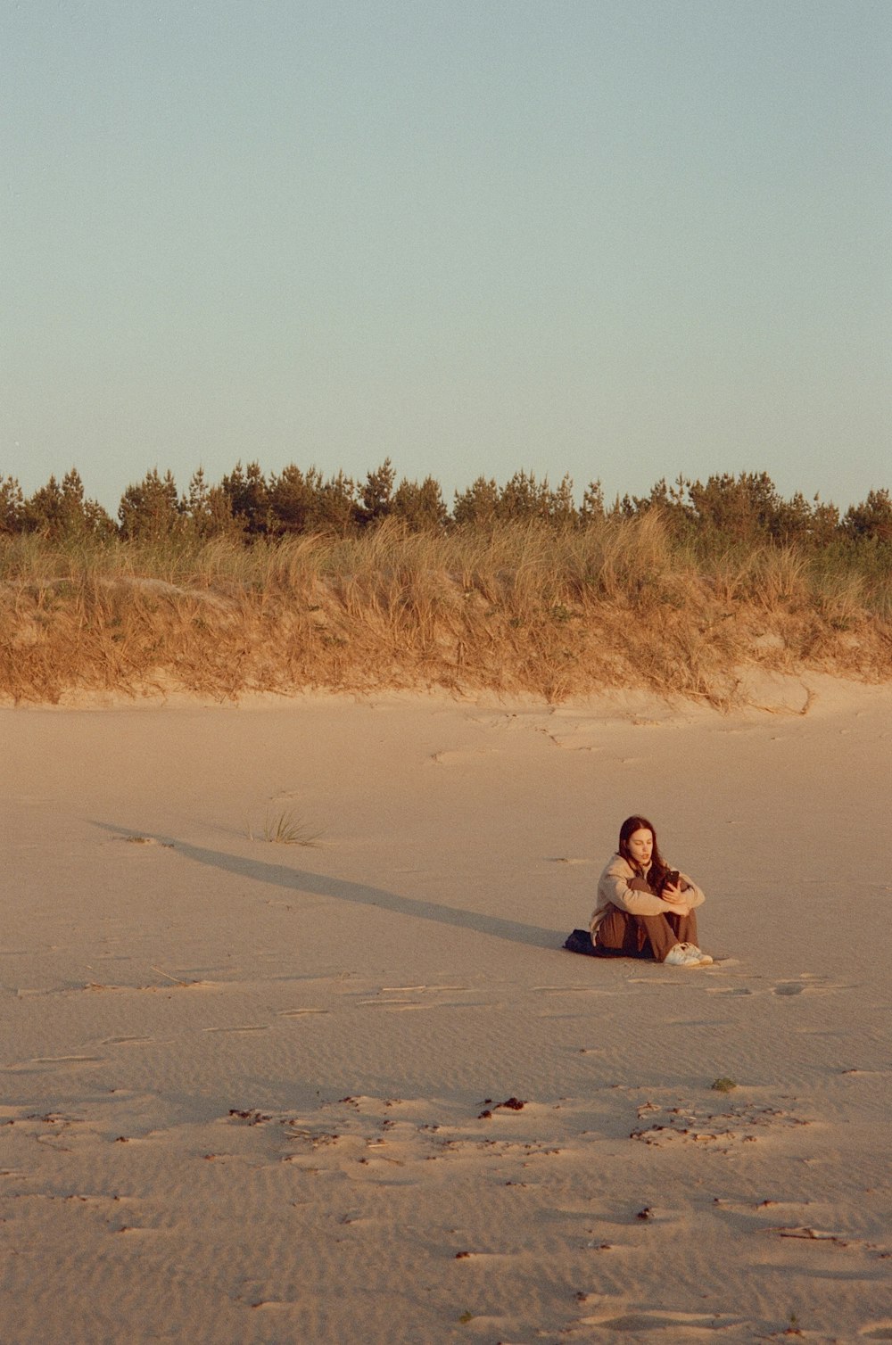 Una mujer sentada en la arena con una cometa en el fondo