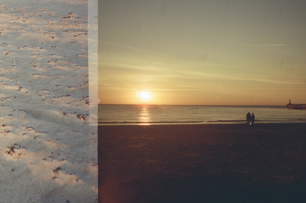 a couple of people standing on top of a sandy beach