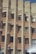 The image features a brick building facade with multiple air conditioning units installed on the walls between the windows. The building has a modern architectural design with uniform, rectangular windows. The brickwork alternates between lighter and darker shades, giving a textured appearance to the structure. There is a slight glare or light reflection visible at the bottom right corner.