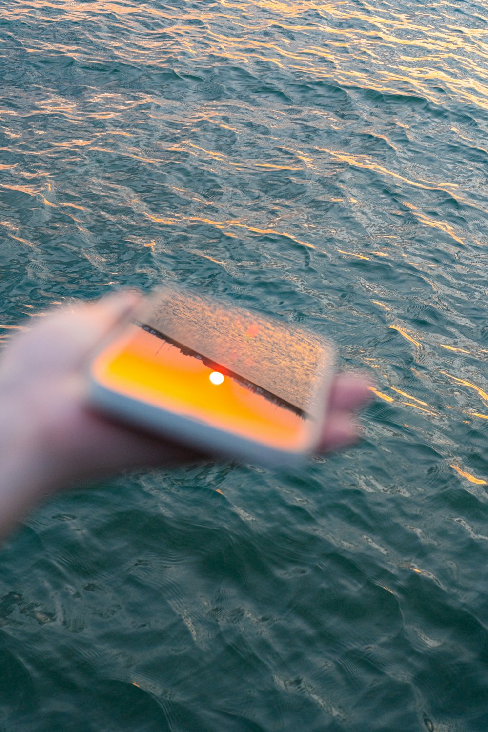 a hand holding a cell phone over a body of water