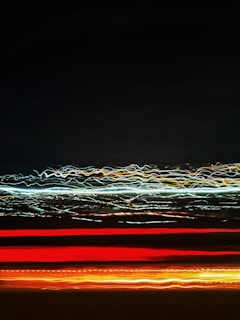 A series of light trails, with red, orange, and white streaks against a dark background, creating an abstract and dynamic visual effect.