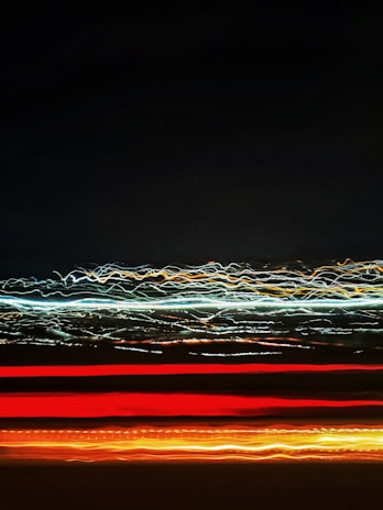 A series of light trails, with red, orange, and white streaks against a dark background, creating an abstract and dynamic visual effect.