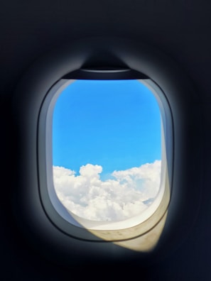 A window view from an airplane showing fluffy clouds and a bright blue sky.