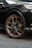 Close-up of a car wheel featuring a stylish alloy rim with orange and silver accents. The wheel is mounted on a dark-colored vehicle, parked on a tiled surface. The design of the rim is modern and sharp, showcasing intricate patterns.