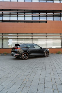 A sleek black sedan parked in front of a modern office building, ready for passenger pickup.