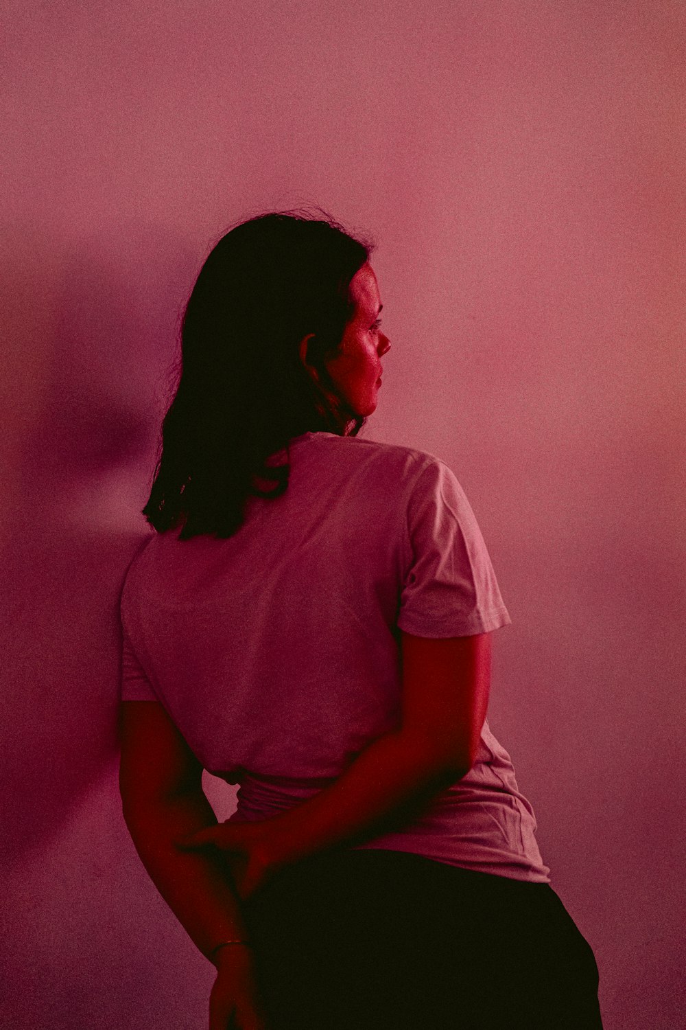 a woman sitting on a stool in front of a pink wall