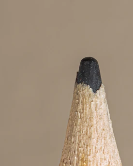 Close-up of a sharpened pencil tip resting on a textured wooden desk.