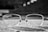 A pair of eyeglasses with rectangular frames rests on a textured stone surface. The background is blurred, giving a sense of depth, and the glasses themselves have visible tiny droplets or marks on the lenses.