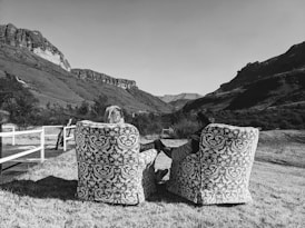 a woman sitting on top of two chairs in a field