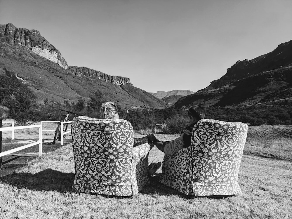 a woman sitting on top of two chairs in a field