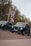 Two black taxi cabs are driving on a street lined with Union Jack flags, surrounded by trees. The vehicles have distinct designs typical of London taxis, with their front grilles prominently visible.