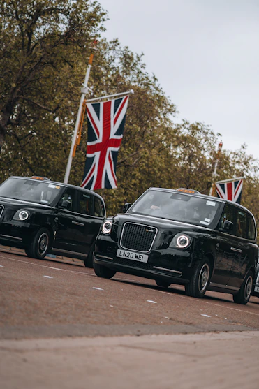 A vibrant London black cab cruising past Tower Bridge with the British flag waving gently in the background.