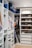 A well-organized walk-in closet featuring neatly arranged clothes on hangers, a set of drawers, and shelves filled with various pairs of shoes. Luggage bags are stored at the top, and a pillow is placed on the upper shelf.