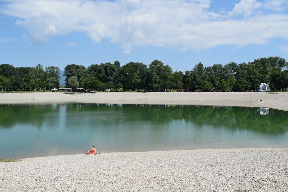 a person sitting in the sand near a lake