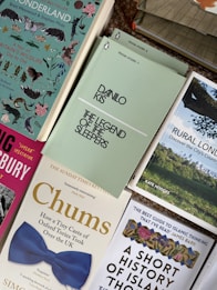 A collection of books arranged in a somewhat overlapping pattern, including titles with varied themes and cover designs such as wildlife, historical analysis, and cultural exploration. Notable titles include 'The Legend of the Sleepers' by Danilo Kis, and 'Chums', which features a distinctive blue bow tie image on its cover.