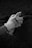 A gloved hand holding a spray paint can against a rough textured surface. The scene appears monochromatic, emphasizing the rugged texture of the wall.