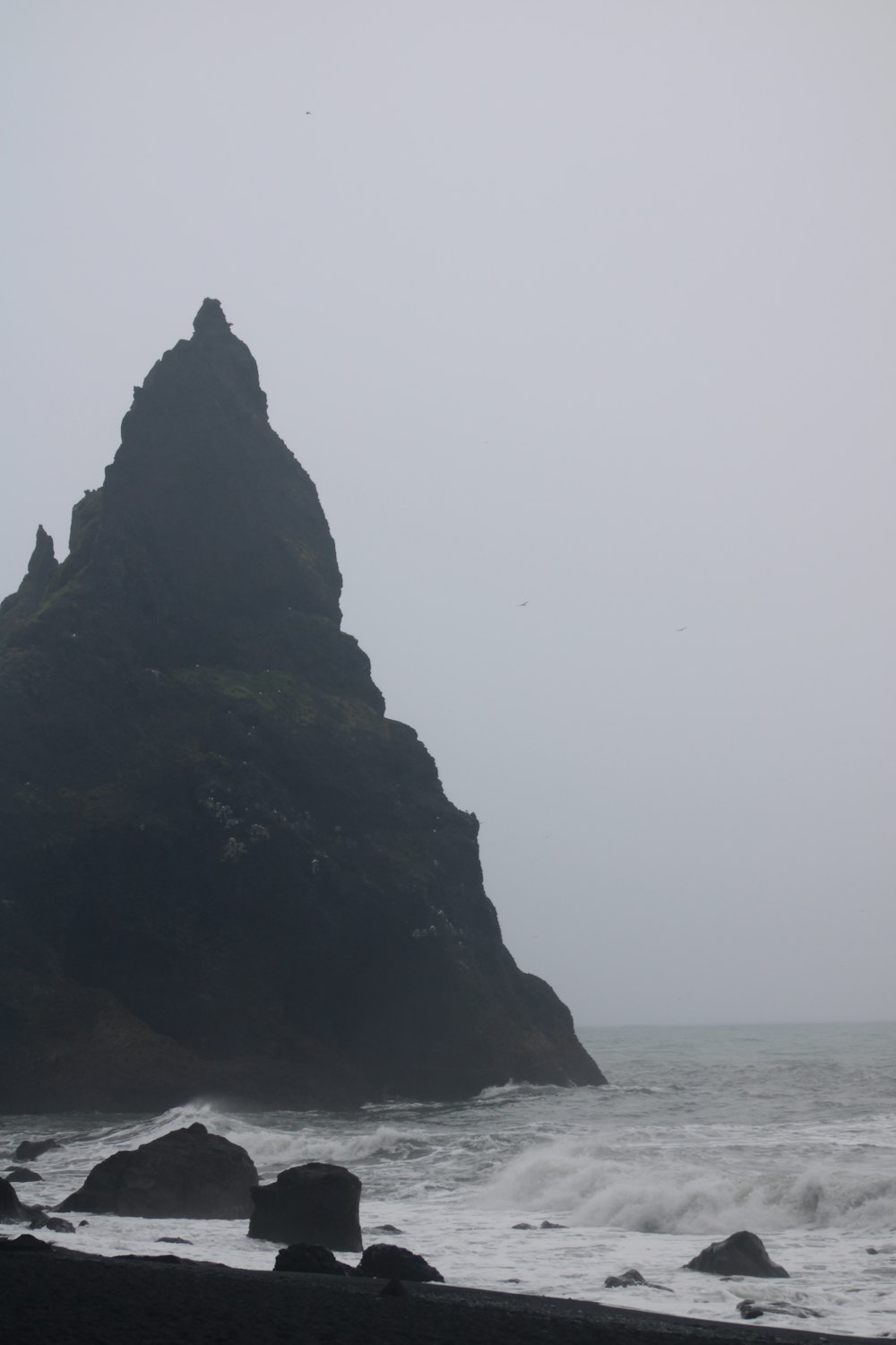 Una gran roca que sobresale del océano en un día de niebla