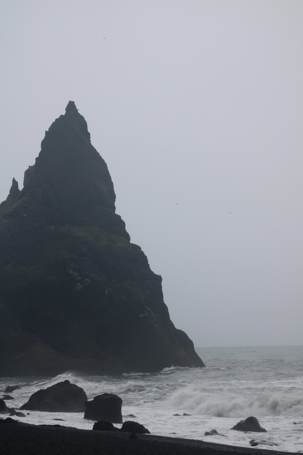 a large rock sticking out of the ocean on a foggy day