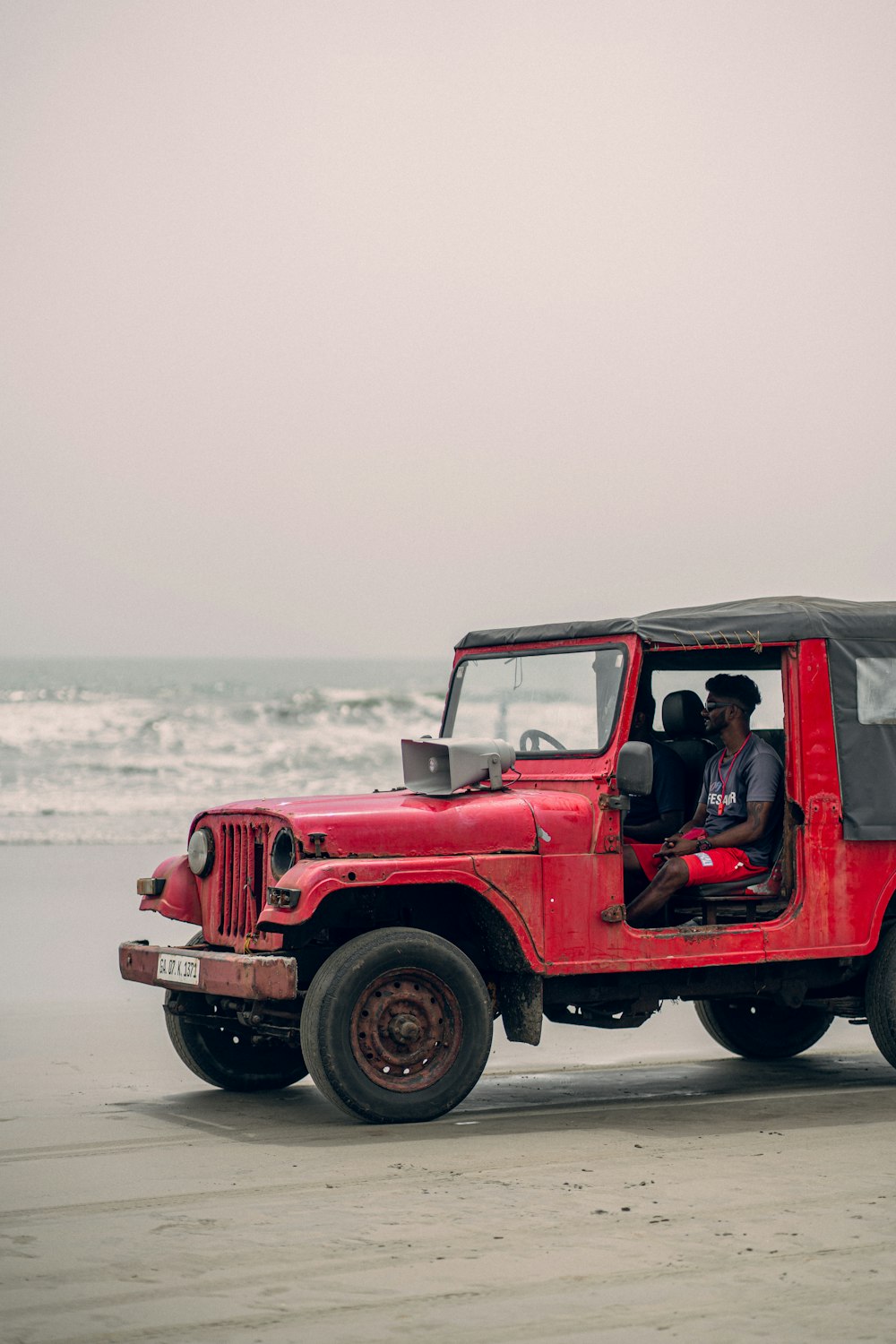 a man driving a red jeep on the beach