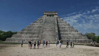 A small group enjoying a private guided tour in front of the Kukulkan Pyramid at Chichen Itza under a bright blue sky.