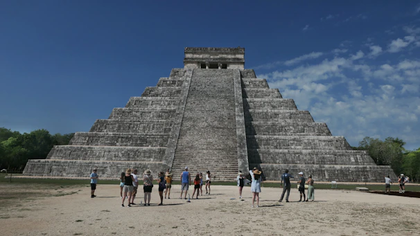 A small group enjoying a private guided tour in front of the Kukulkan Pyramid at Chichen Itza under a bright blue sky.