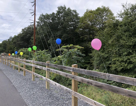 Colorful balloon garland twisting around a rustic wooden frame at a garden party.