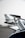 A detailed view of a car spoiler or wing with a sleek metallic and aerodynamic design in the foreground. In the background, a blurred image of an airplane is visible, suggesting a location at an airport or airstrip. The environment appears overcast with soft lighting.