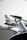 A detailed view of a car spoiler or wing with a sleek metallic and aerodynamic design in the foreground. In the background, a blurred image of an airplane is visible, suggesting a location at an airport or airstrip. The environment appears overcast with soft lighting.