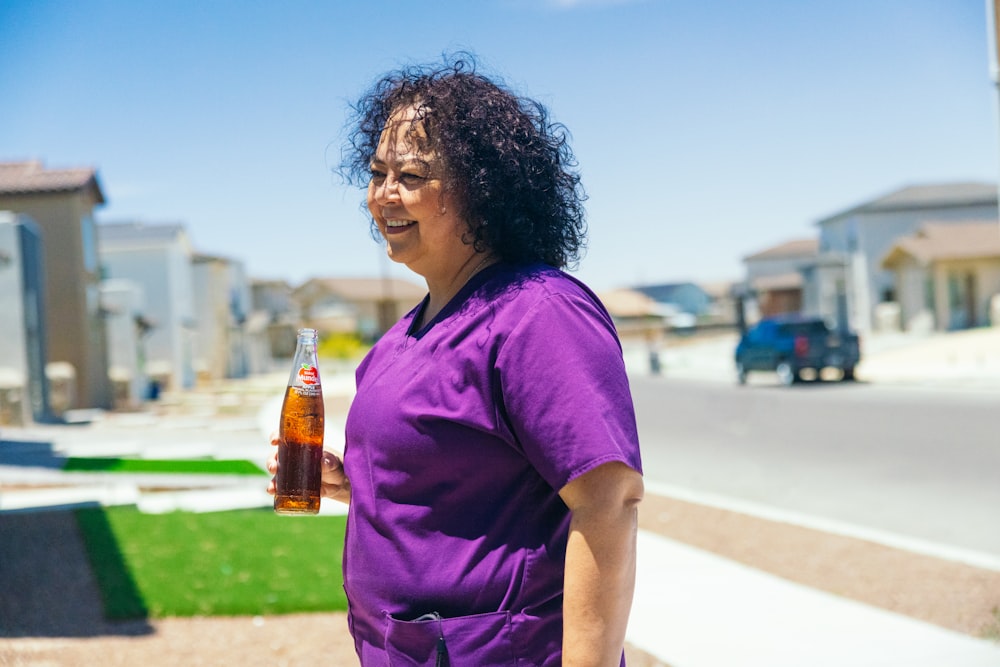 a woman in a purple shirt holding a bottle of beer