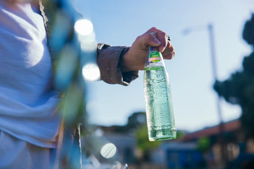Hand holding a chilled juice bottle with droplets of condensation in a sunny outdoor setting.