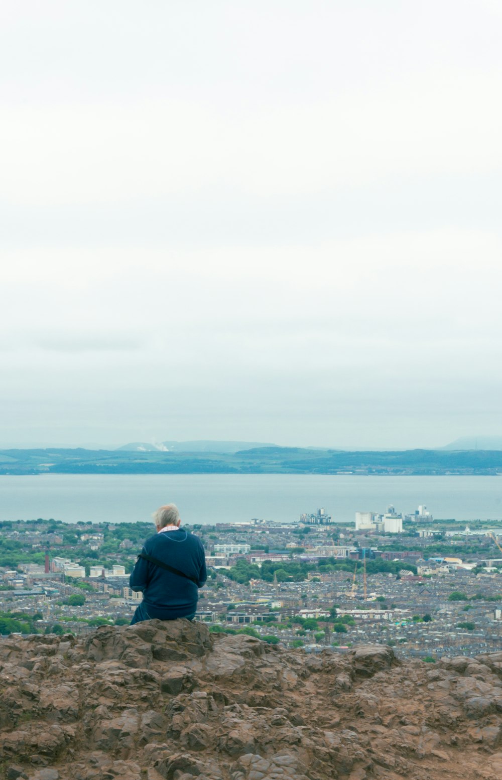 a man sitting on top of a hill overlooking a city