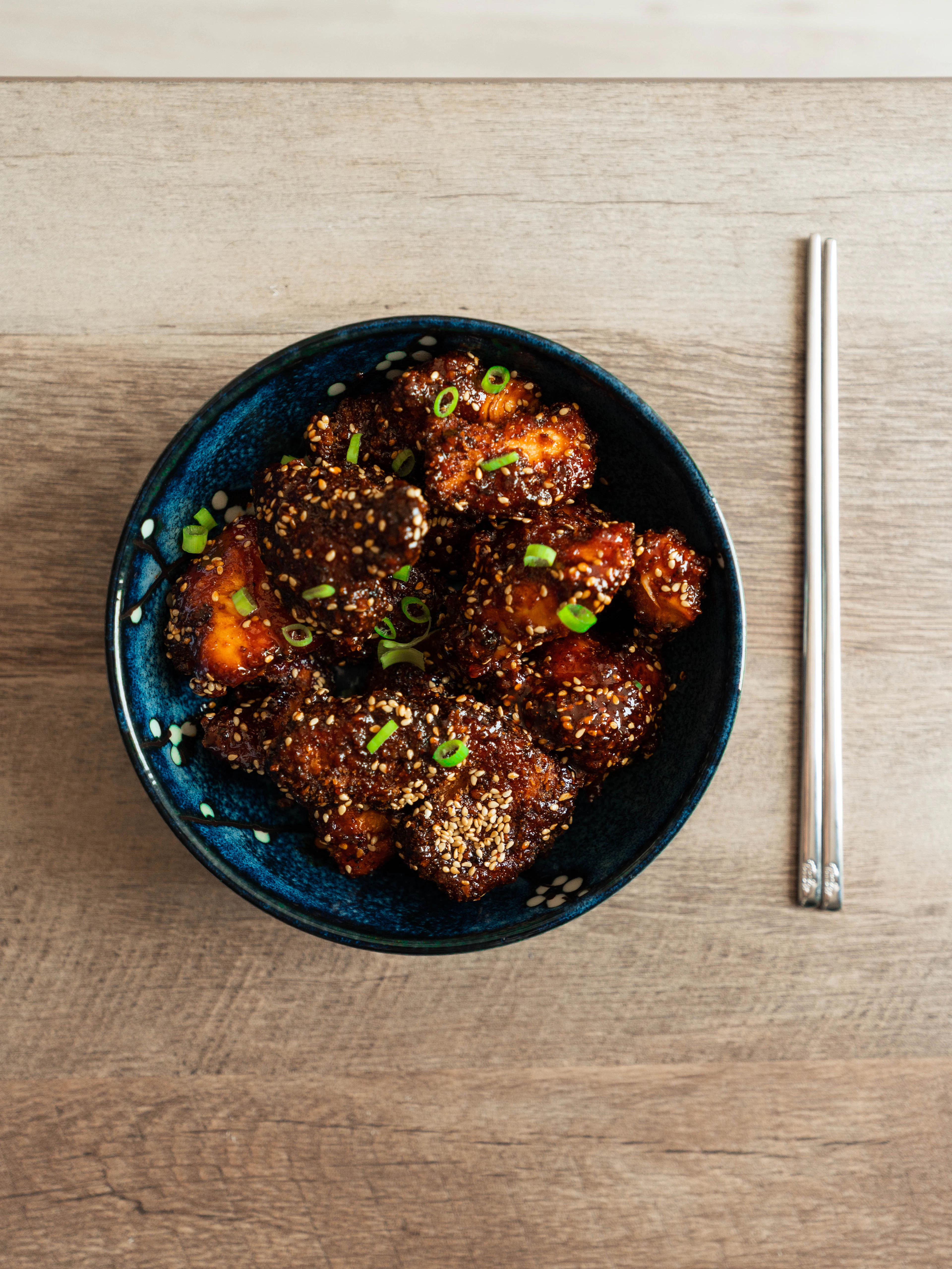 Glazed Korean fried chicken with sesame seeds and green onion in a blue bowl