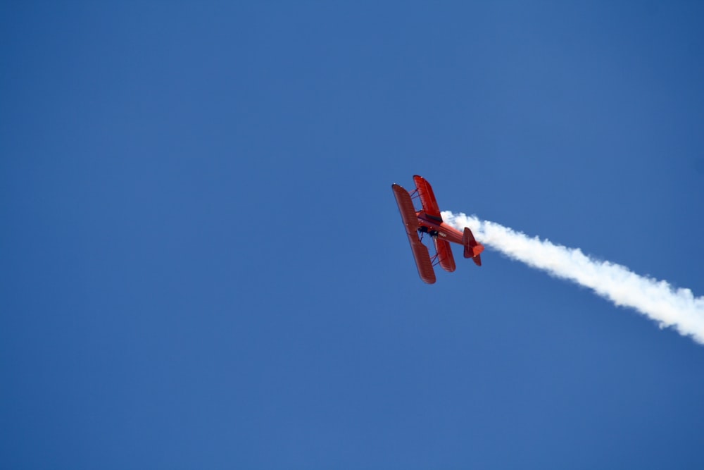 a red plane flying in the sky leaving a trail of smoke behind it