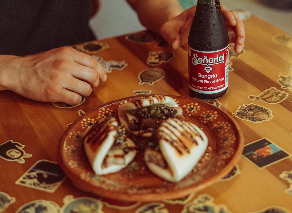 eine Person, die mit einem Teller Essen und einer Flasche Bier an einem Tisch sitzt