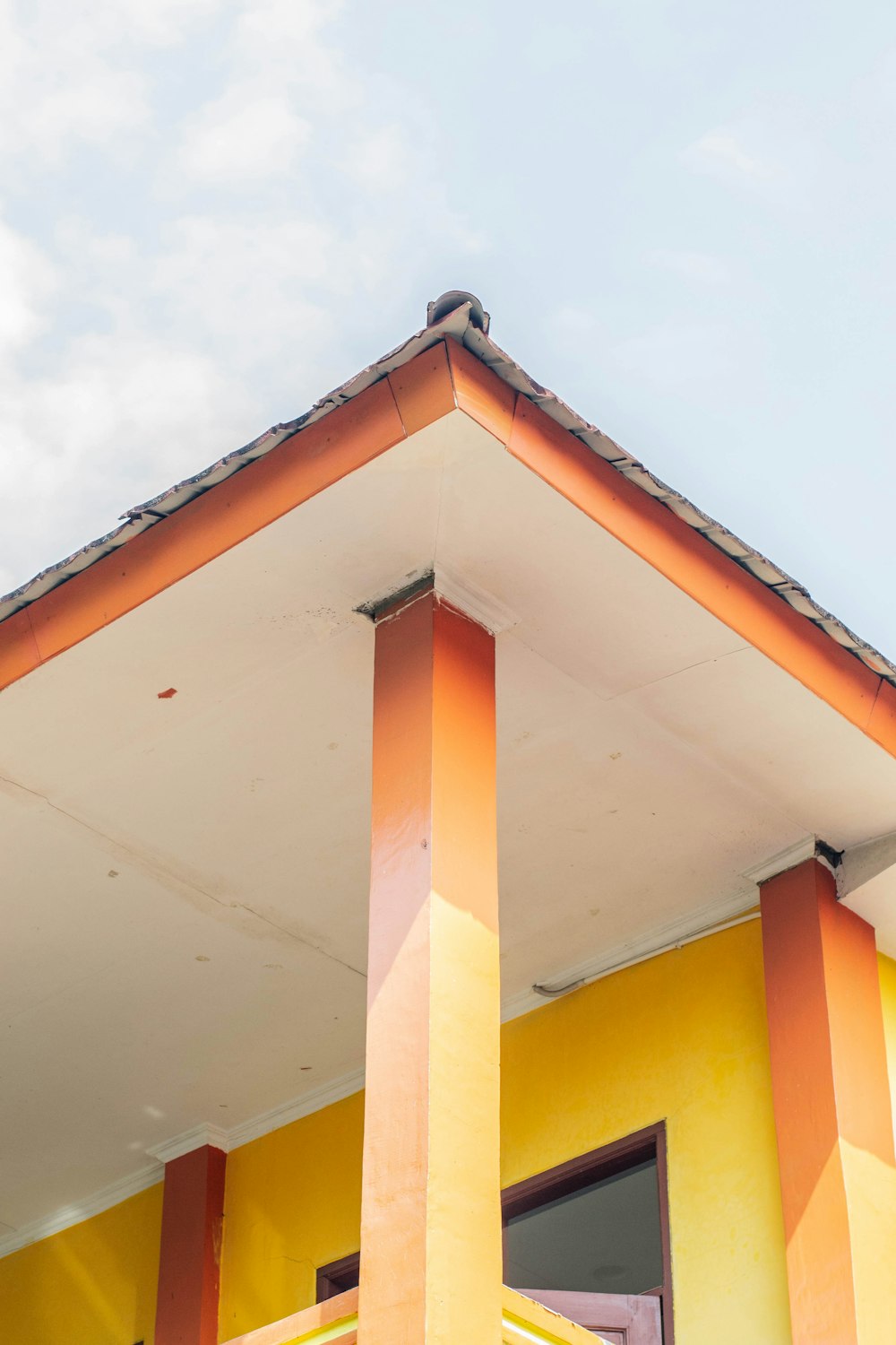 a yellow building with a red roof and two windows