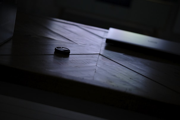 A sleek black Bluetooth tracker resting on a modern wooden table with soft natural light.