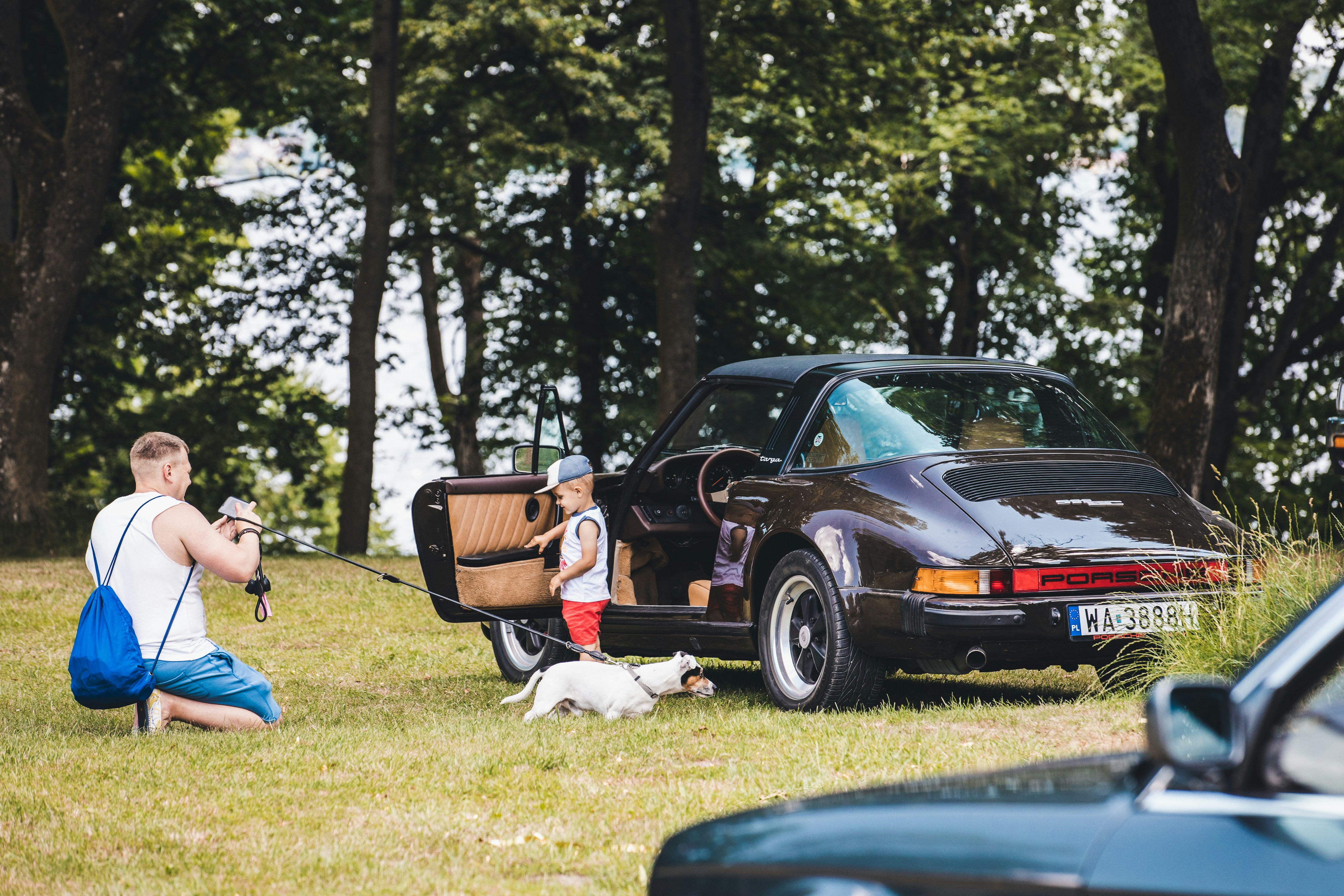a man kneeling down next to a car with a dog on a leash