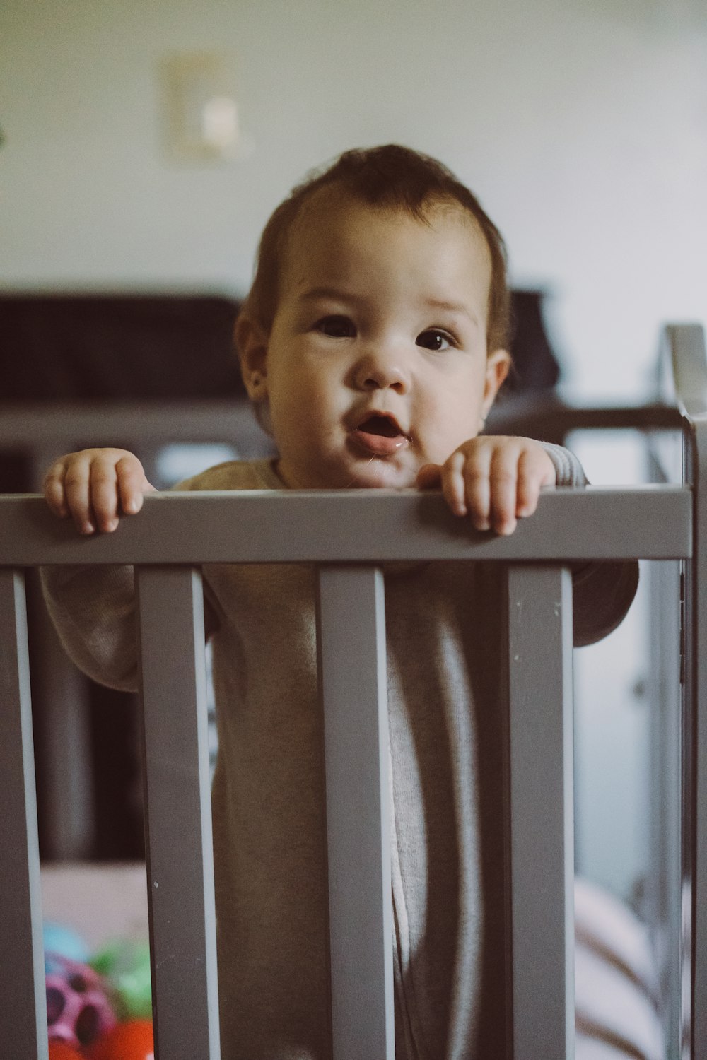 a baby standing in a crib looking at the camera