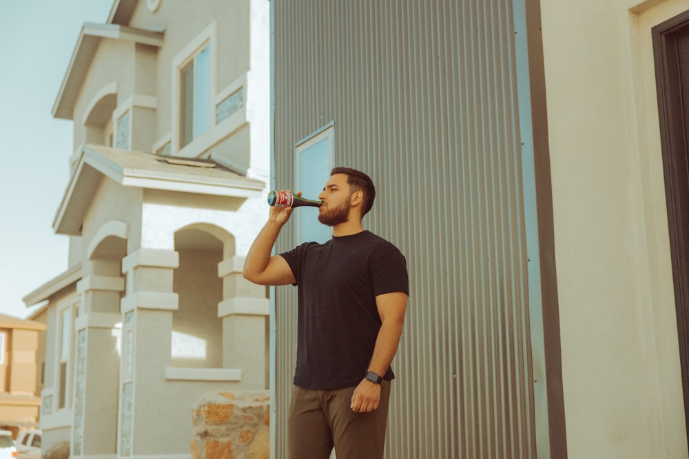 a man standing outside of a building drinking from a bottle