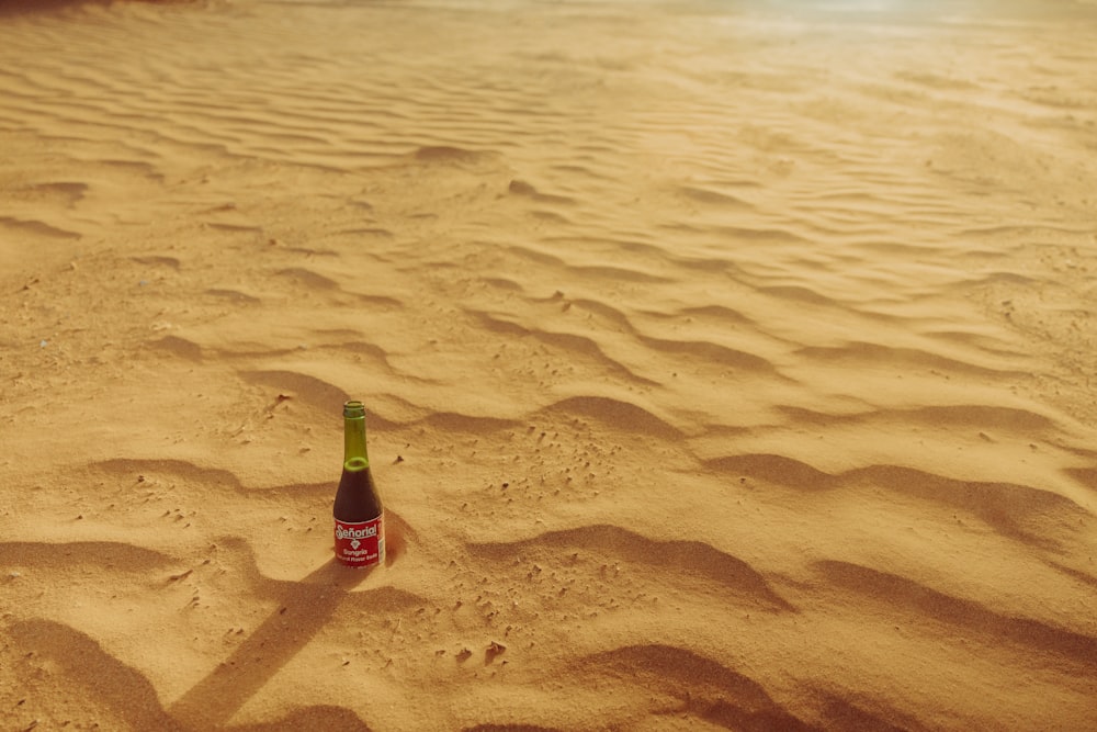 a bottle of beer sitting on top of a sandy beach