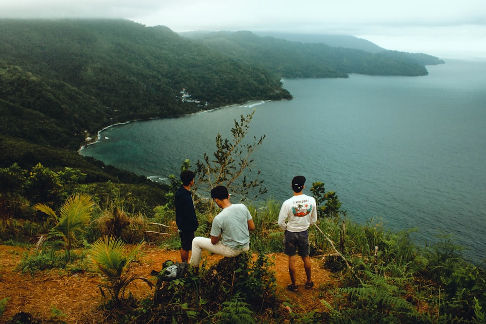 three people sitting on a hill overlooking a body of water