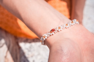 A graceful bracelet featuring soft pink and sage green beads arranged on a warm cream background with a tiny ladybug perched on the side