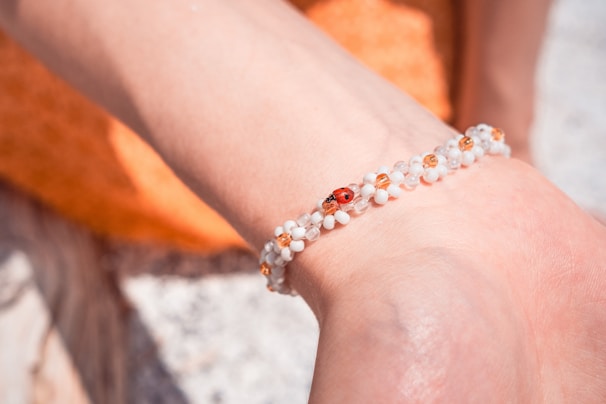 A graceful bracelet featuring soft pink and sage green beads arranged on a warm cream background with a tiny ladybug perched on the side