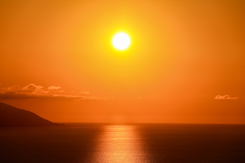 the sun is setting over the ocean with a boat in the water