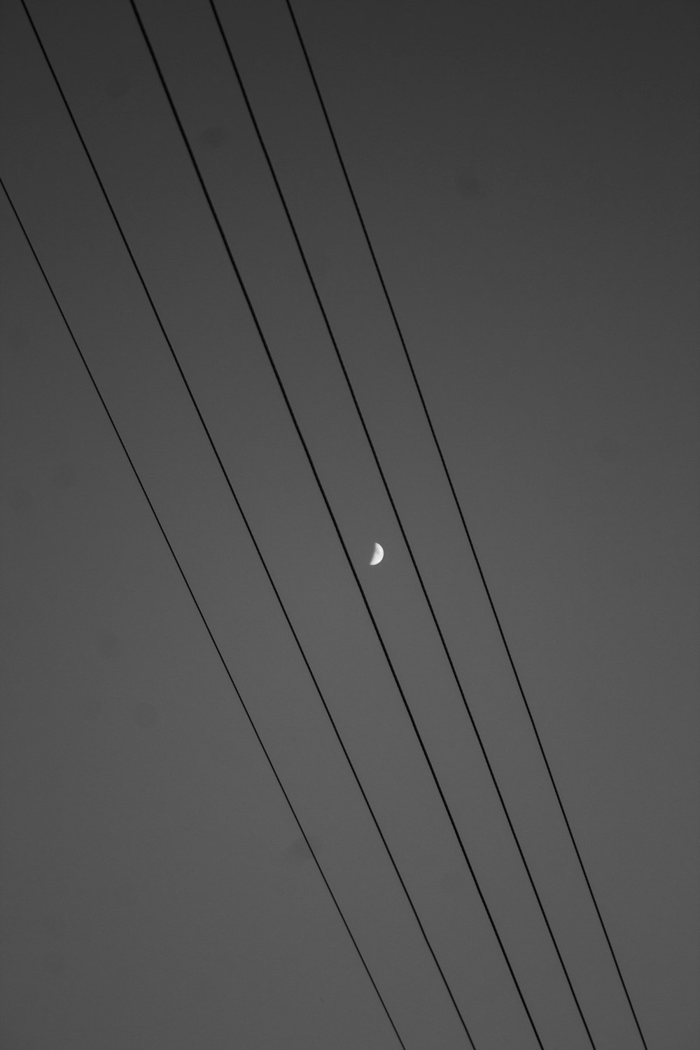 a black and white photo of power lines with the moon in the distance