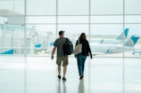 A traveler and companion smiling with backpacks at an airport lounge.
