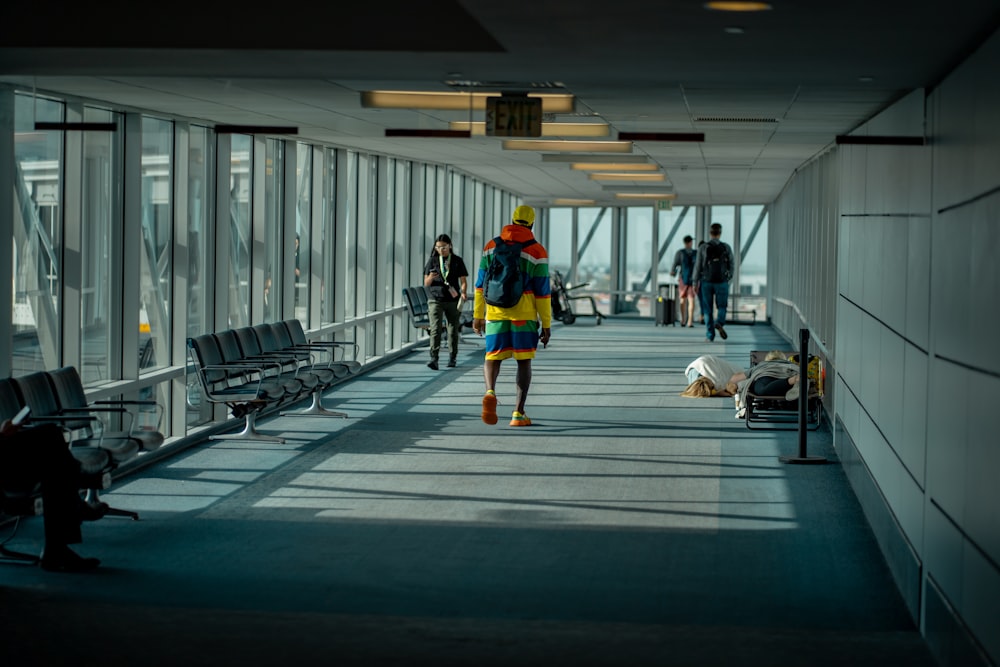 a man walking down a long hallway with lots of windows