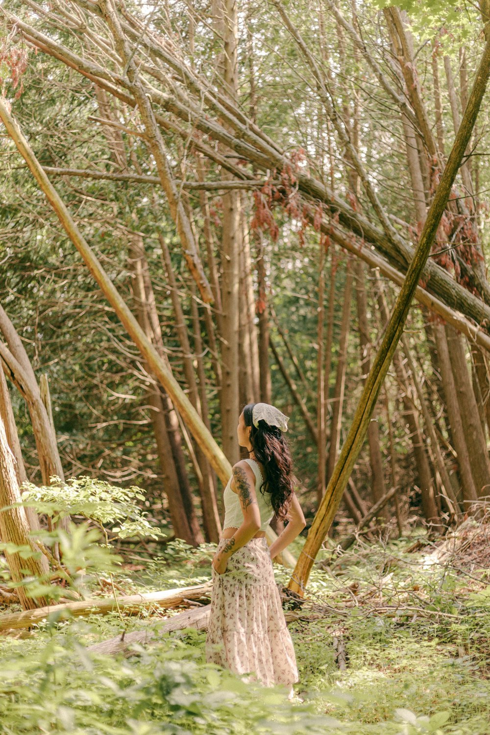 a woman in a dress and hat standing in the woods