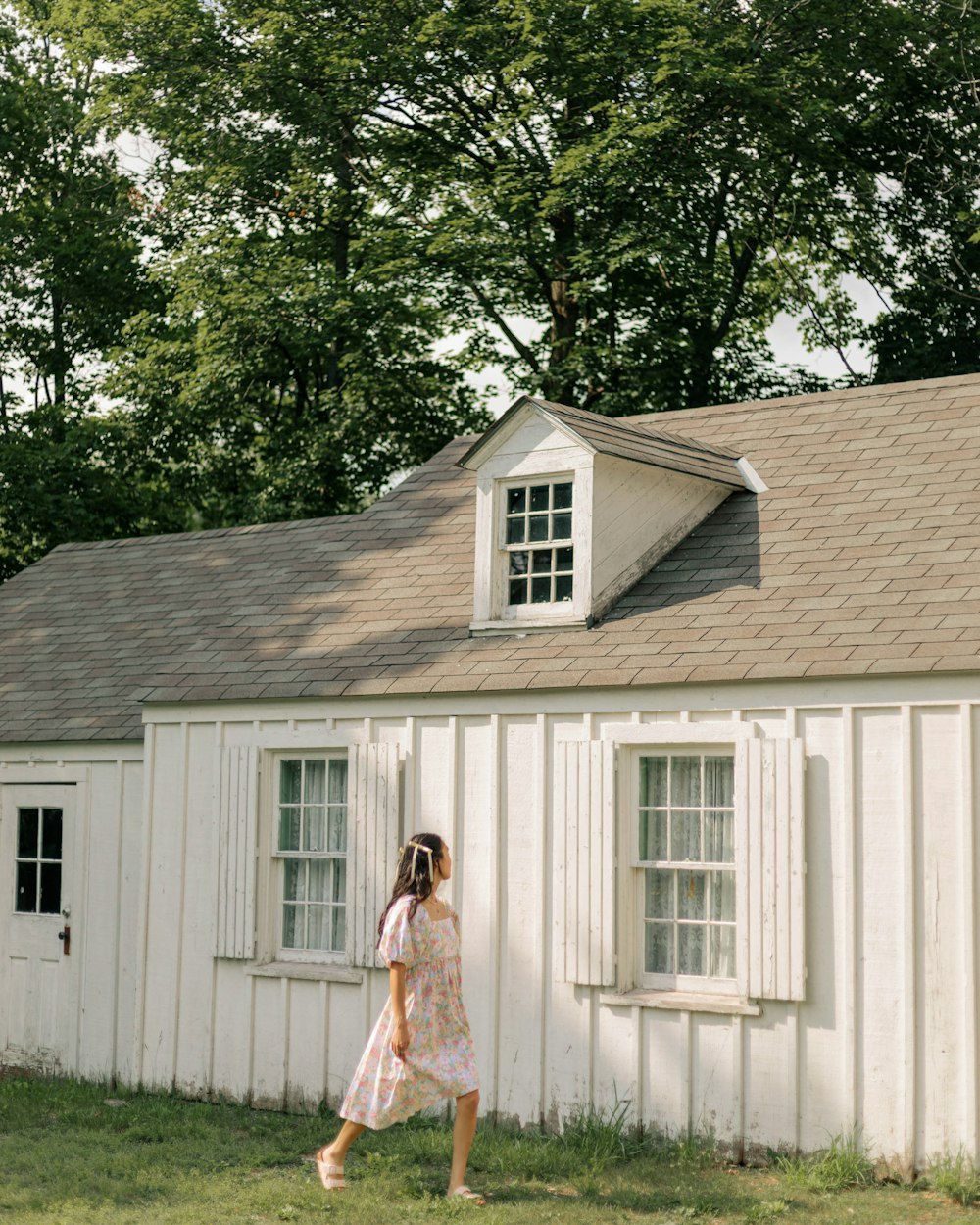 a woman walking past a white building in a field